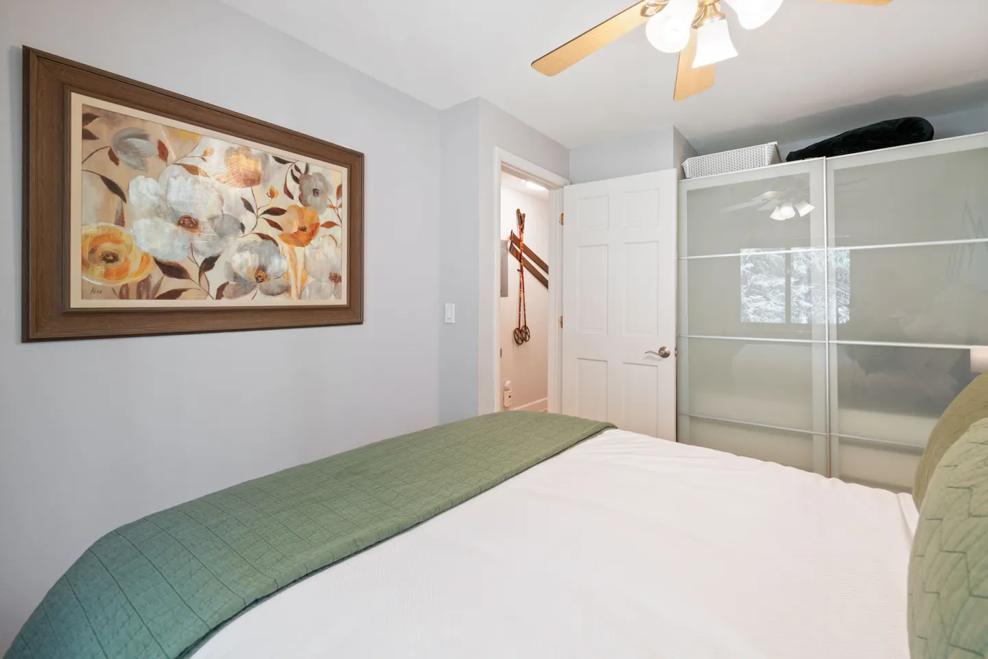Bedroom featuring a made bed with green accents, framed floral artwork, a ceiling fan, and frosted glass sliding wardrobe doors.