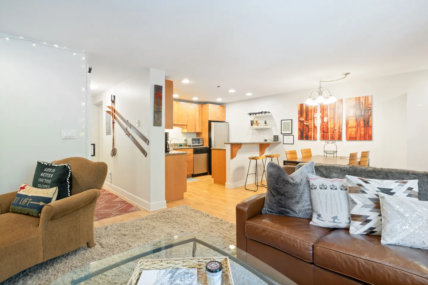 Open-concept living room with leather sofa leading to kitchen and dining area with ski-themed decor