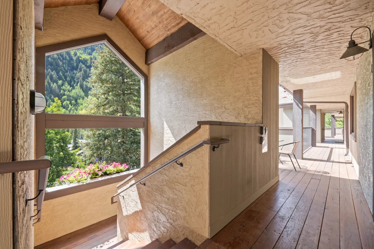 Stairwell landing leading to an outdoor breezeway with wood-plank flooring and views of forested mountains.