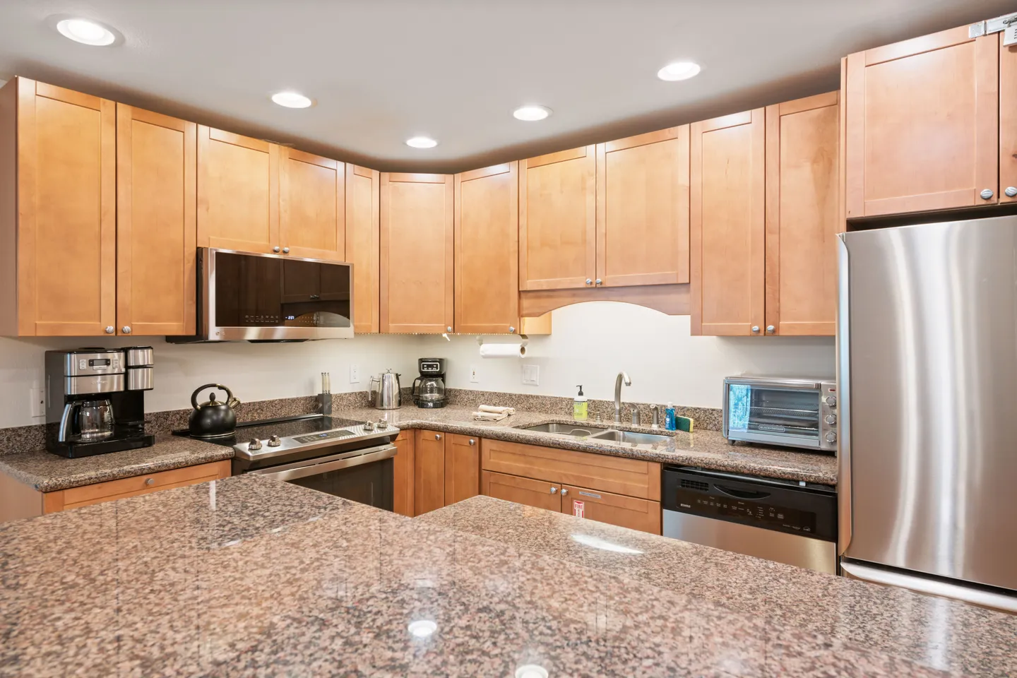 Kitchen with wooden cabinetry, speckled granite countertops, and stainless steel appliances.