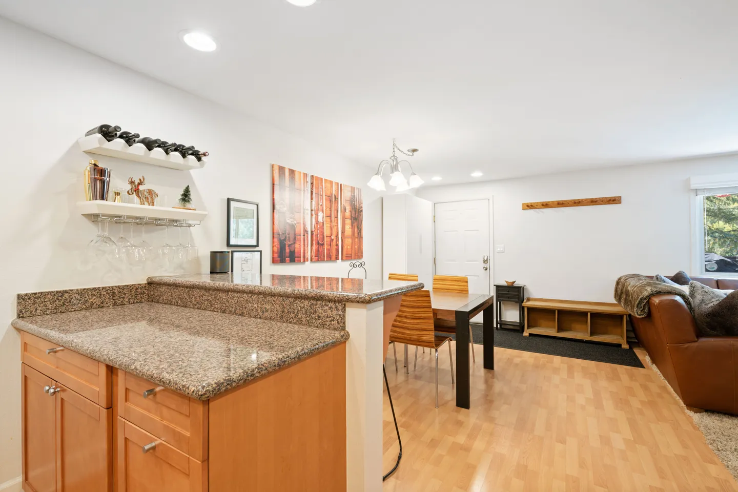Open-concept interior showing kitchen counter with granite-style surface in the foreground, dining table with chairs, and living area entrance.