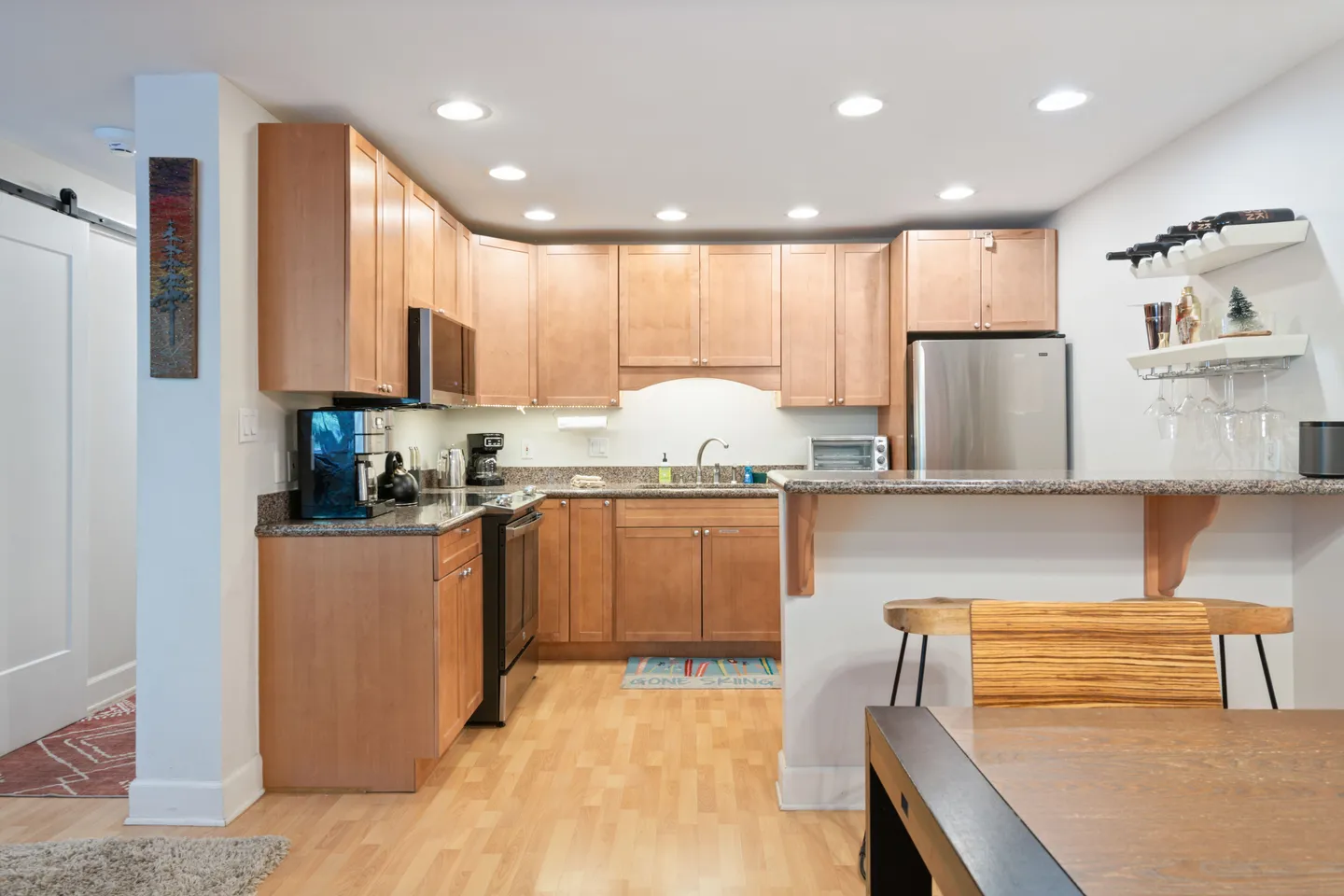 Kitchen with wooden cabinetry, speckled countertops, stainless steel appliances, and a breakfast bar next to a dining table.