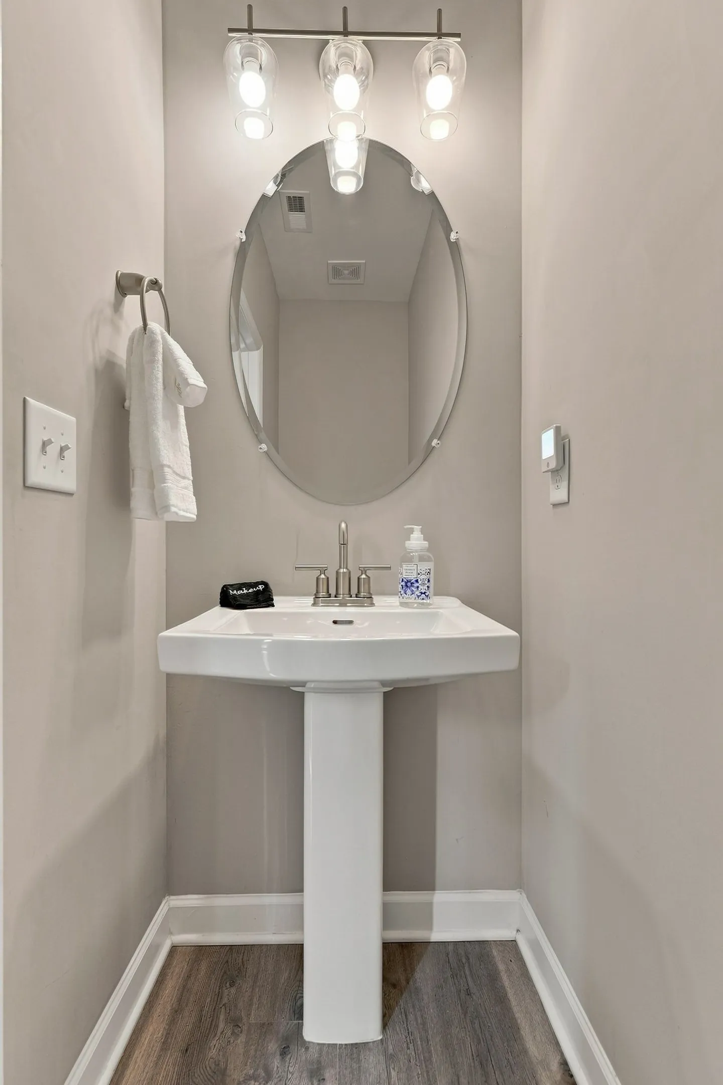 A pedestal sink with an oval mirror and a three-light fixture in a powder room alcove.