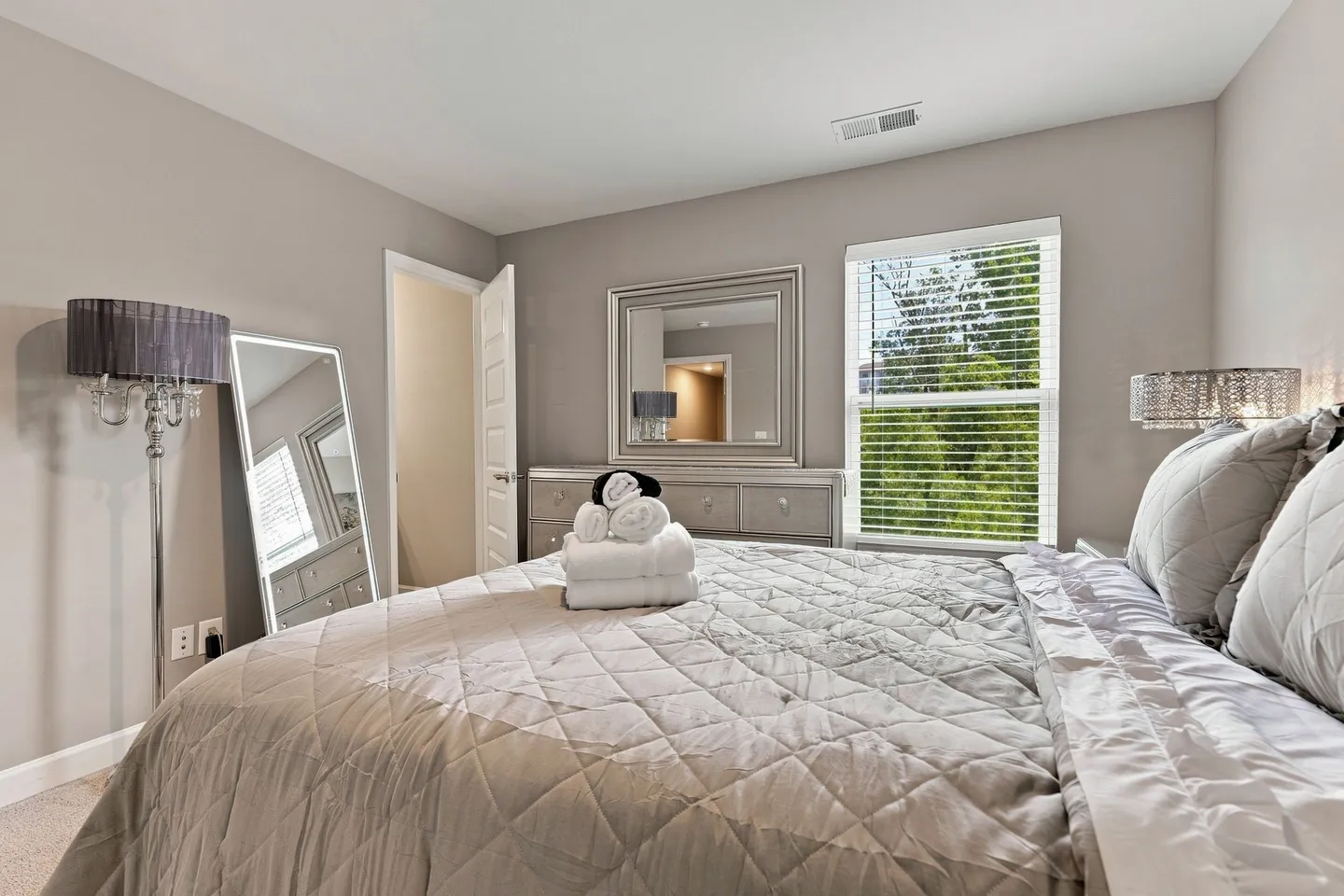 Bedroom featuring a made bed with a quilted coverlet, rolled towels, a dresser with mirror, and a full-length floor mirror.