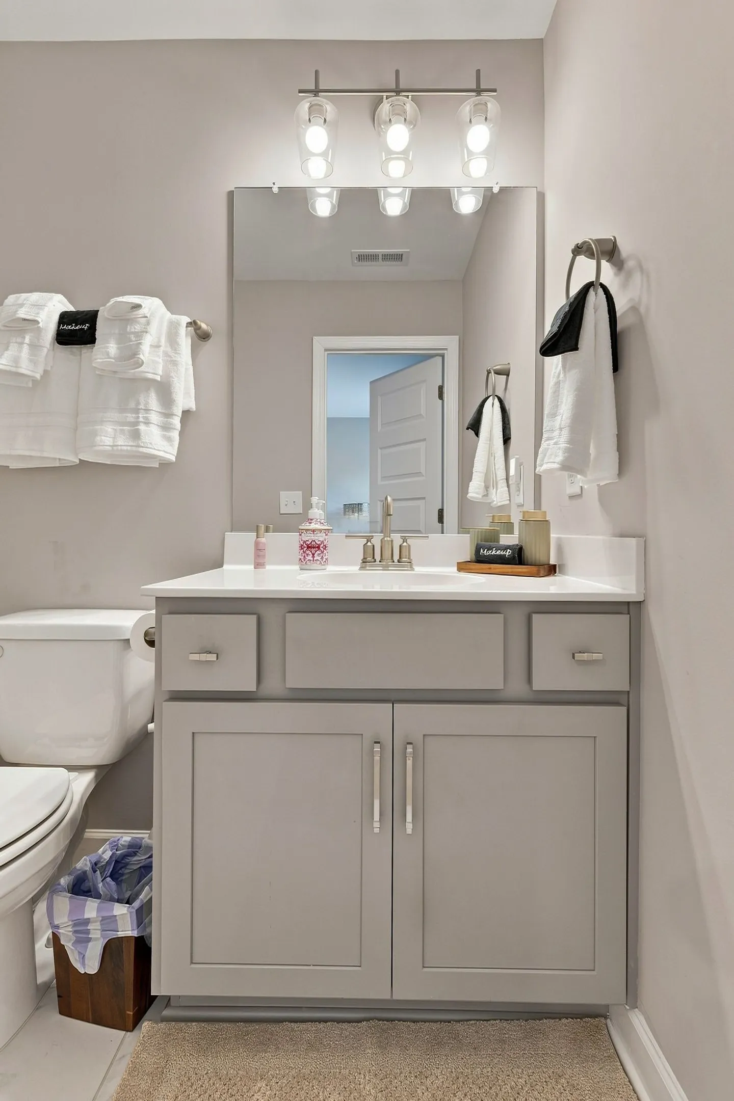 Bathroom with a light gray vanity, white countertop, rectangular mirror, modern light fixture, and adjacent toilet.