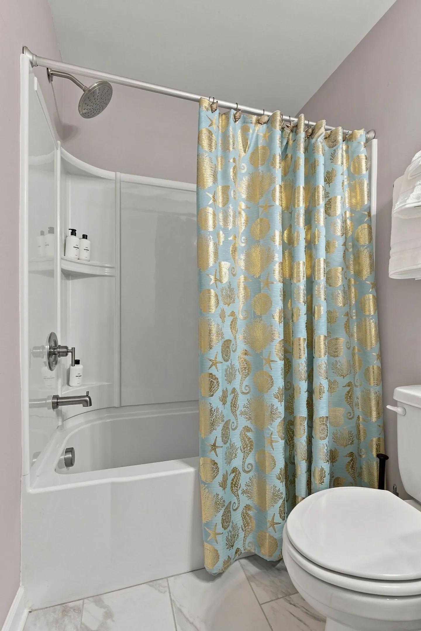 Bathroom with a white tub and shower combination, a light blue and gold patterned shower curtain, and a white toilet.