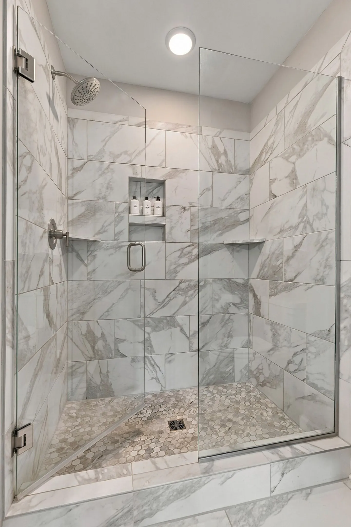 Walk-in shower with marble-look wall tiles, hexagon mosaic floor tiles, and a clear glass door.