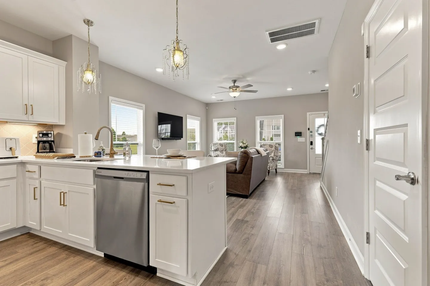 Open-concept kitchen and living area with white cabinets, stainless steel dishwasher, island, and wood-look flooring.