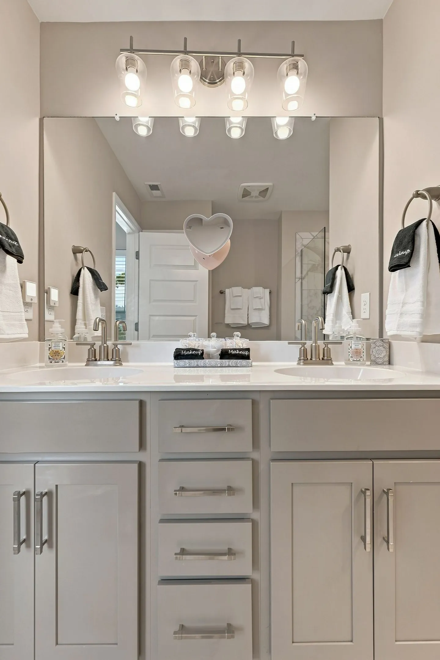 Bathroom double vanity with gray cabinets, white countertop, large mirror, and four-bulb light fixture overhead.