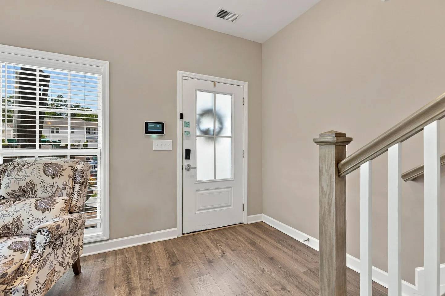 Front entryway with a white front door featuring frosted glass, wood-look flooring, neutral walls, and a staircase railing.