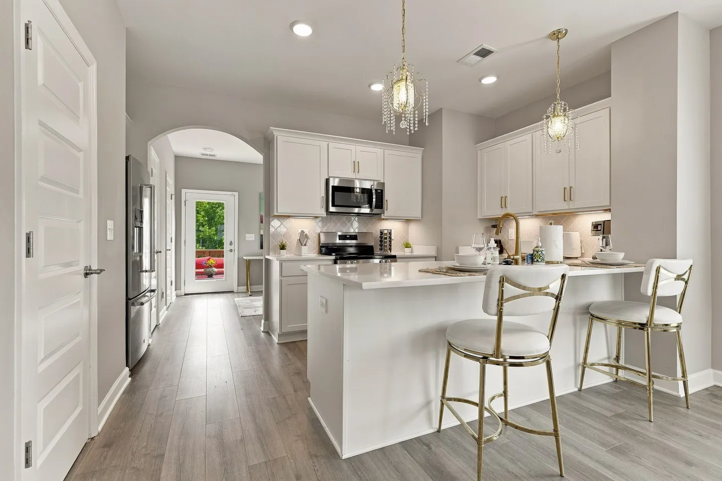 Modern kitchen with white shaker cabinets, light countertops, a breakfast island with two white barstools, and stainless steel appliances.