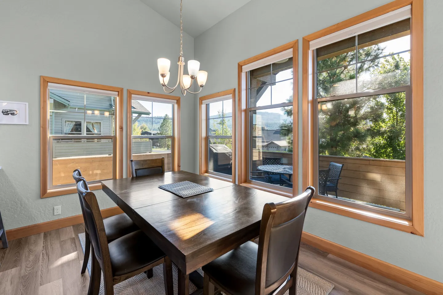 Dining area with a dark wood table and chairs surrounded by wood-framed windows looking out to a balcony.