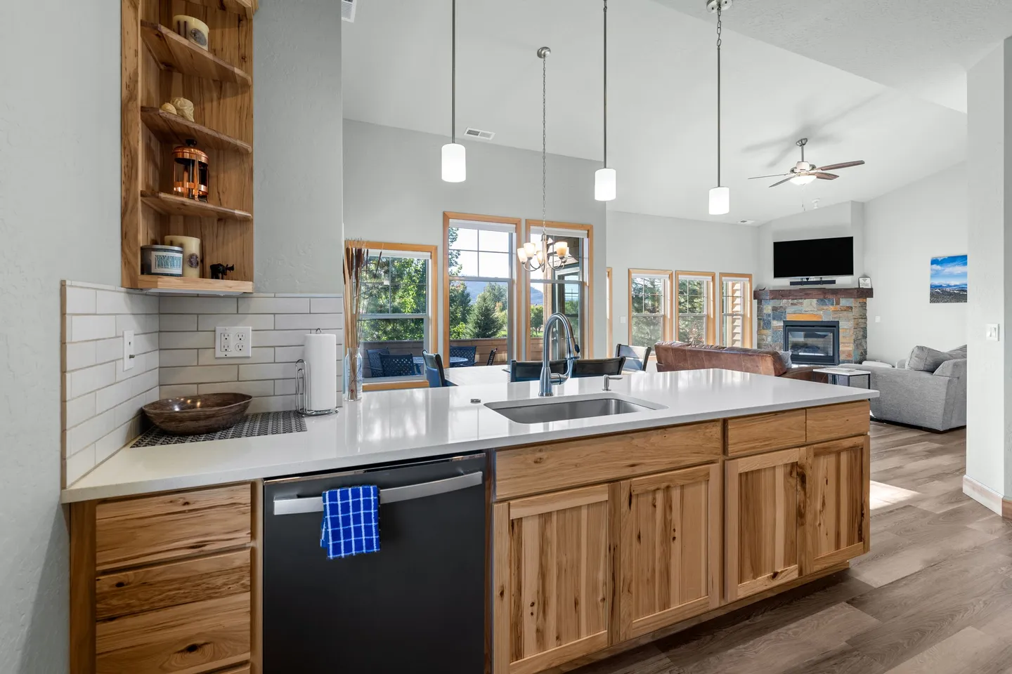 Kitchen island with wooden cabinets and white countertops looking through to the open dining and living area.