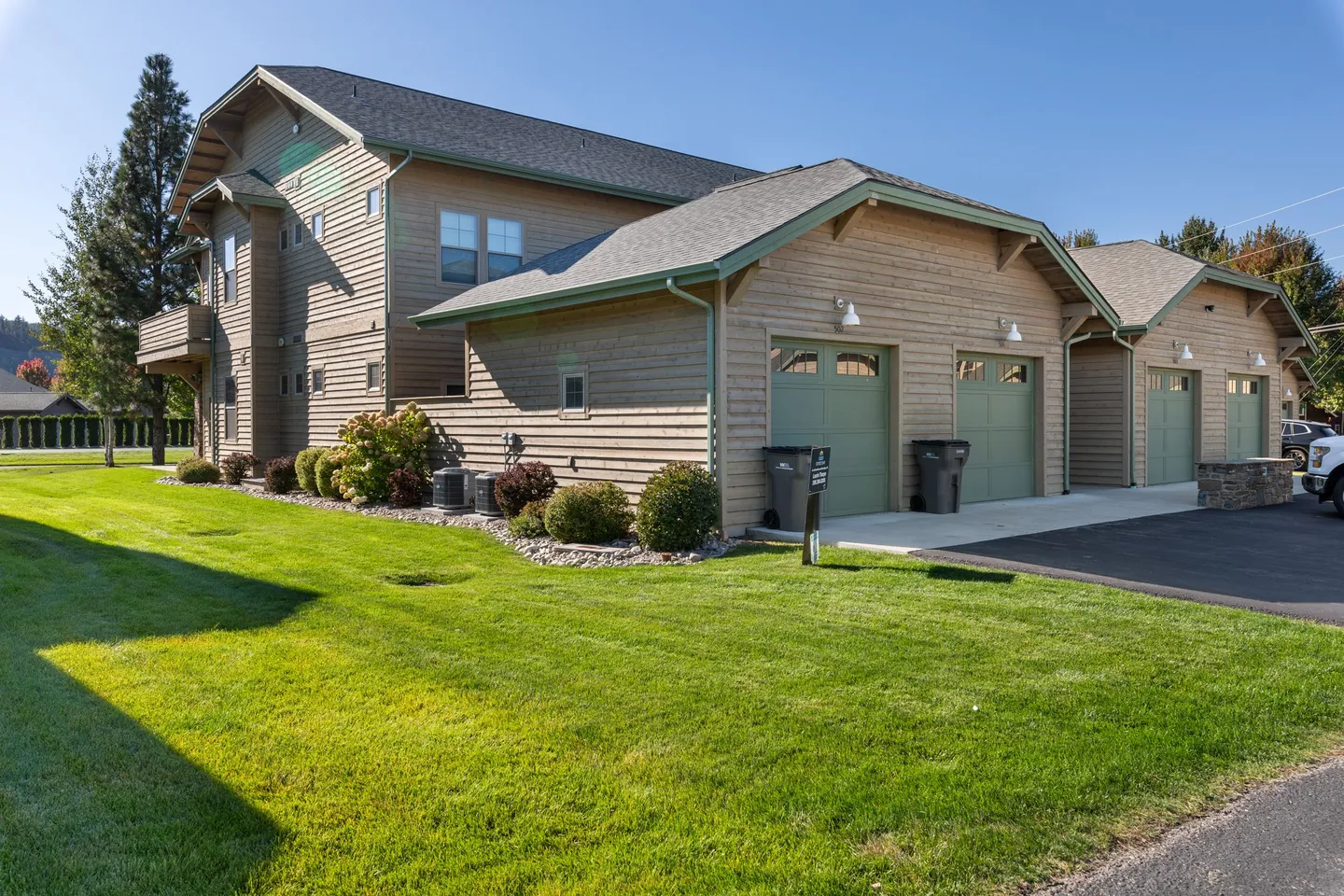 Exterior of a two-story multi-unit building with attached garages, green garage doors, and a manicured green lawn.