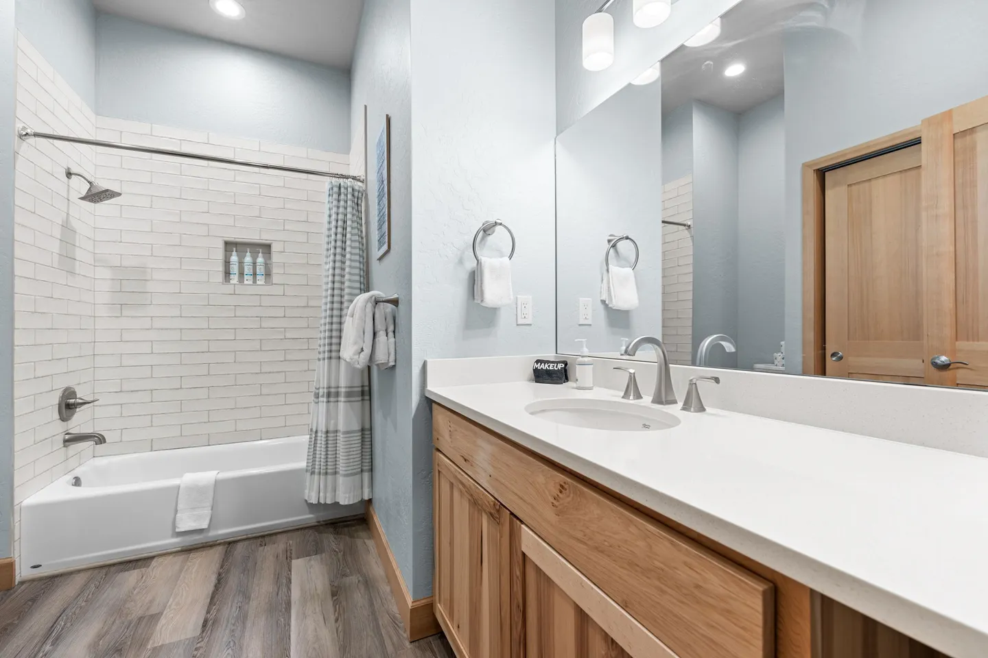 Bathroom with a wood vanity, white countertop, large mirror, and a tub/shower combo with white subway tile.
