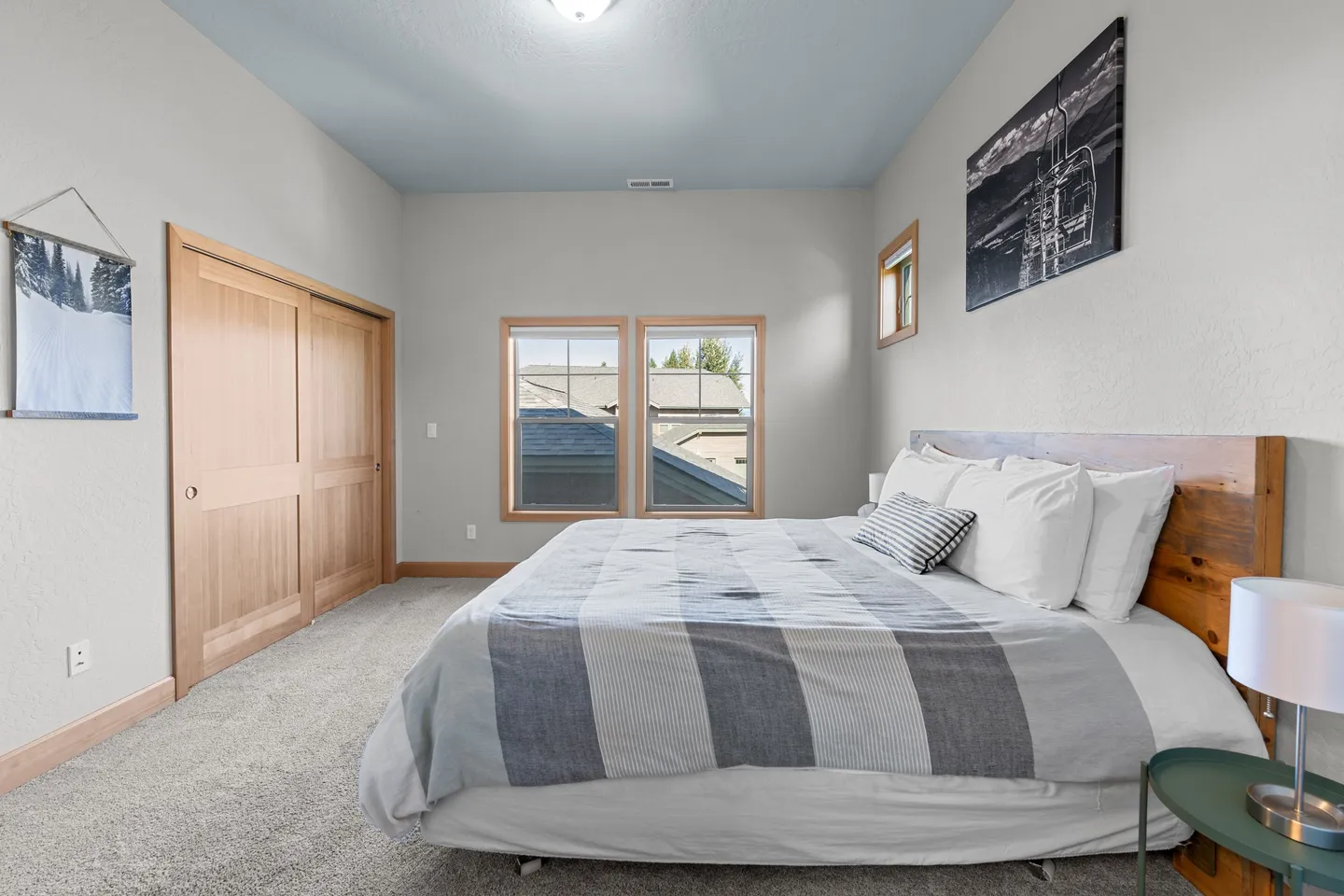 Bedroom featuring a made bed with a wooden headboard, carpeted floor, two windows, and sliding wooden closet doors.