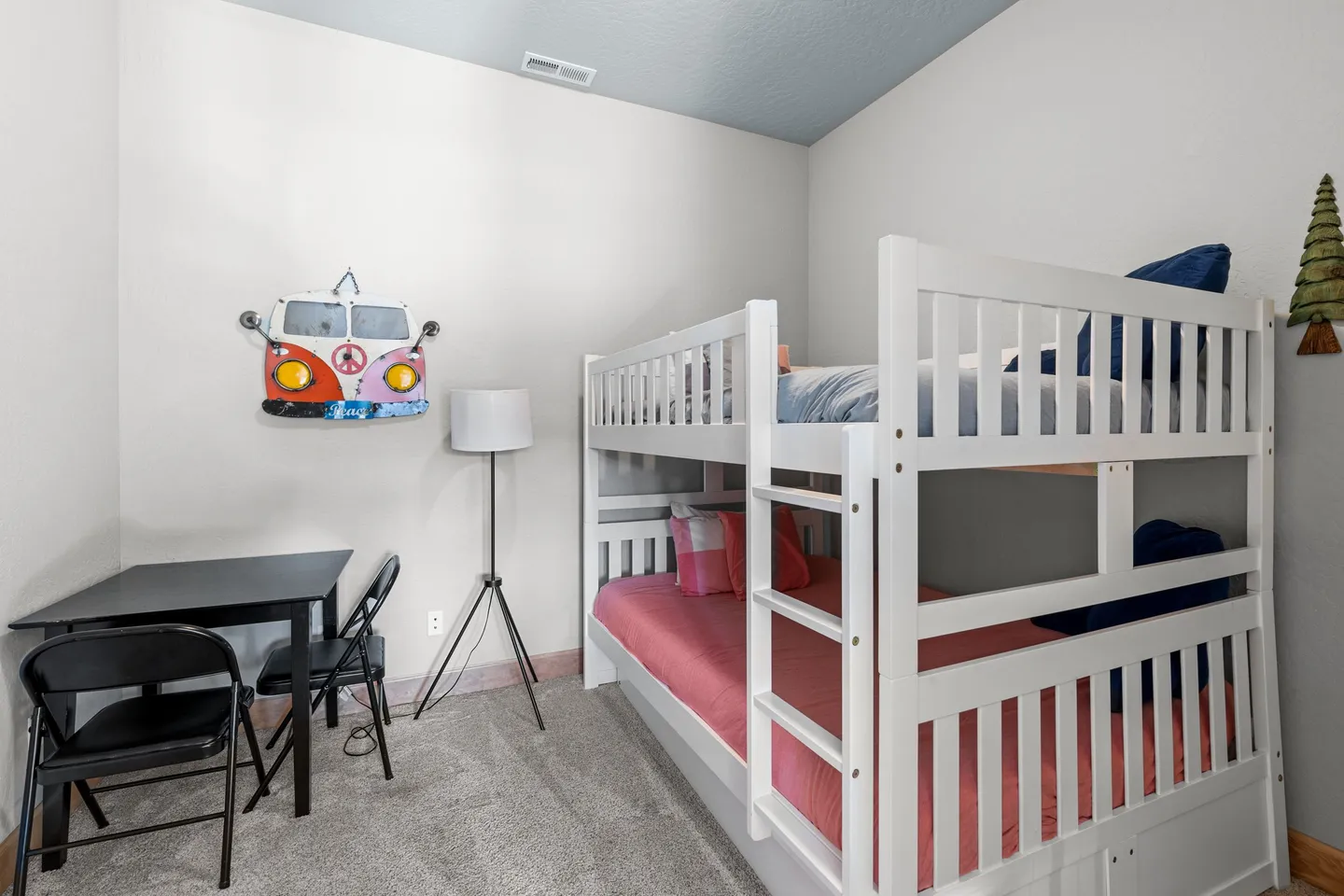 Bedroom featuring a white wooden bunk bed, a small black table with two folding chairs, and carpeted flooring.