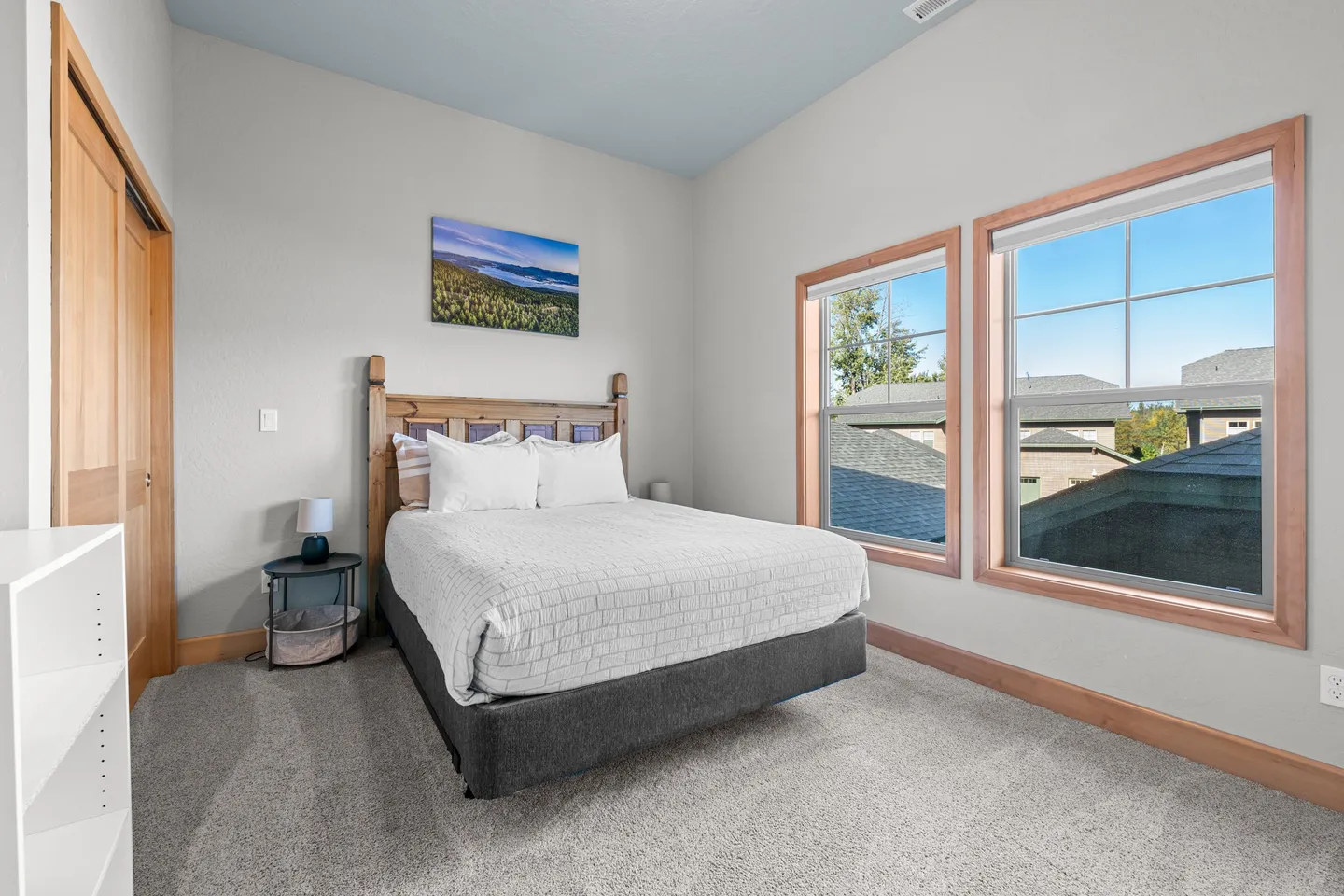 Bedroom with carpet, a wooden headboard, two windows with wooden trim, and a small bedside table.