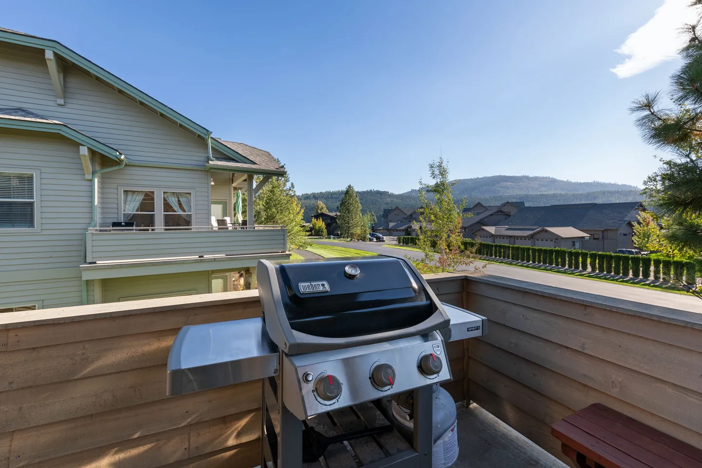A barbecue grill situated on an elevated outdoor deck overlooking a residential street with distant hills under a clear blue sky.