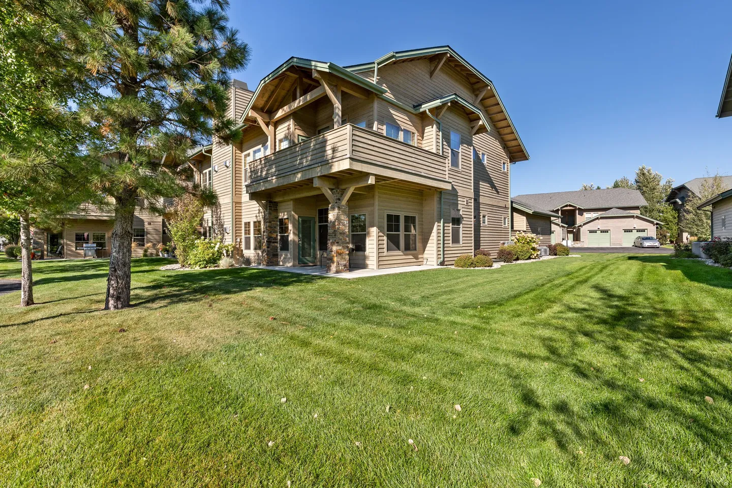 Exterior rear view of a two-story home with siding, an upper balcony, stone-accented pillars, and a green lawn under a clear sky.