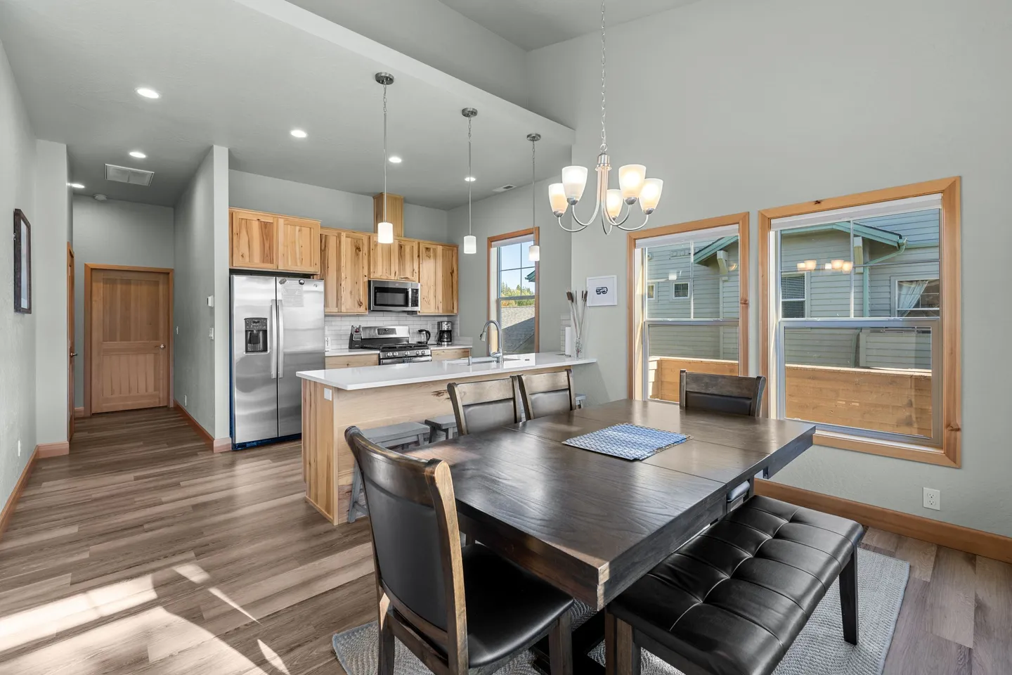 Dining area with dark wood table and tufted bench, opening to kitchen with island and stainless steel appliances.