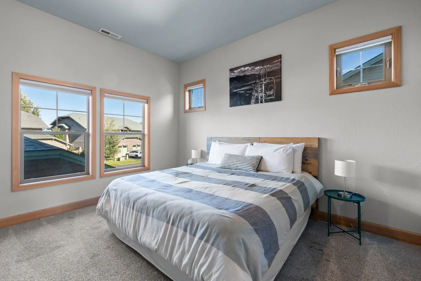 Bedroom with carpet, striped blue and white bedding on a wood-headboard bed, and multiple windows.