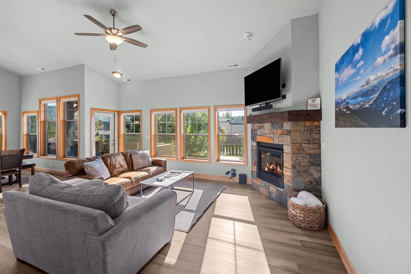 Living room with vaulted ceiling, stone fireplace with mounted TV, and seating near large windows.