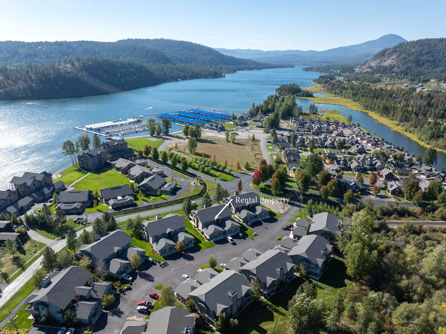 Aerial view of a lakeside residential community with a marina, forested hills, and a home marked Rental Property.