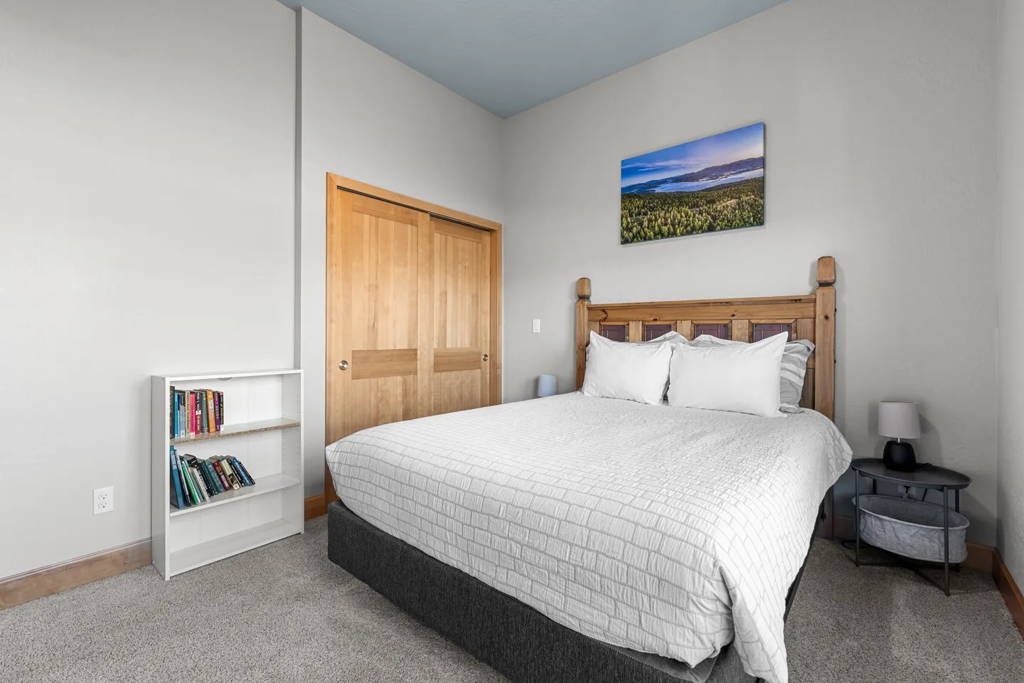 Bedroom with a wooden headboard, white bedding, small nightstand, bookshelf, and sliding wooden closet doors.