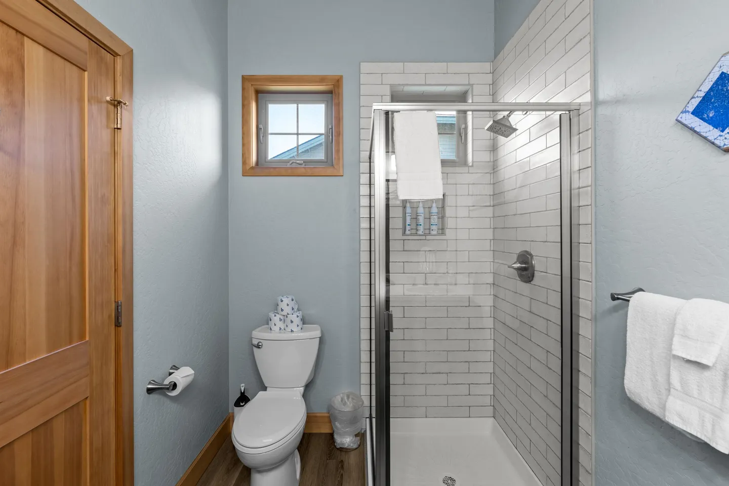 Bathroom with a glass-enclosed walk-in shower tiled in white subway tile, a white toilet, and light blue walls.