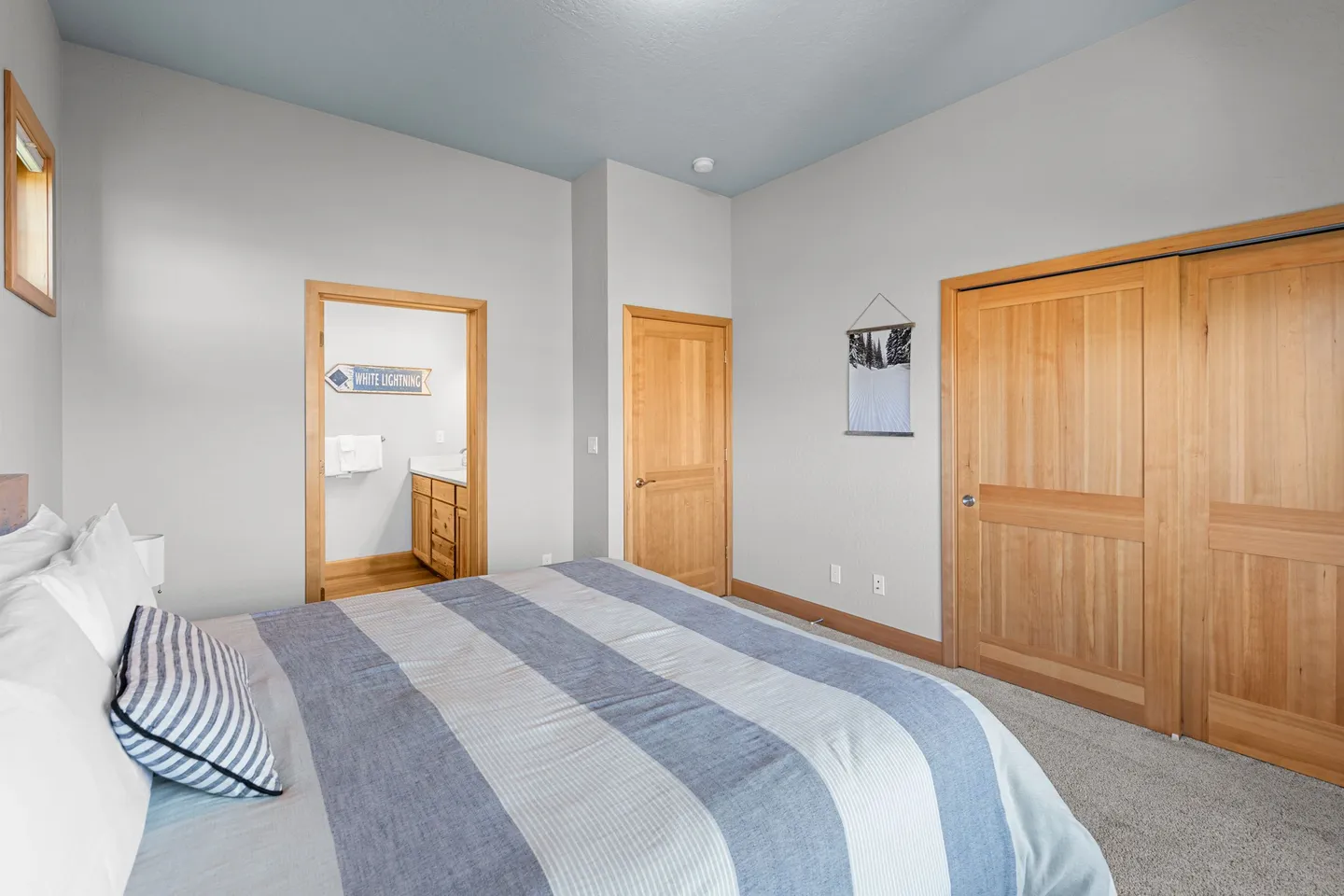 Bedroom with a bed made with blue and white striped bedding, carpeted floor, wood-paneled closet doors, and an open doorway leading into an en-suite bathroom.