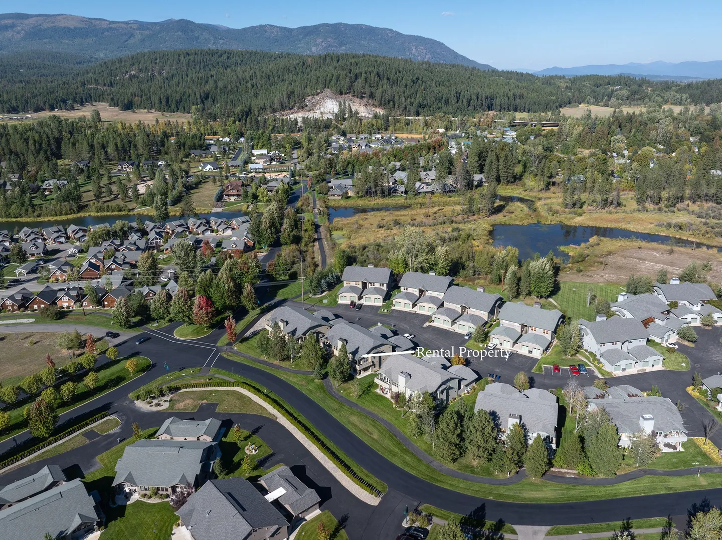 Aerial view of a residential neighborhood with townhomes, ponds, and forested mountains in the background, with an arrow indicating the rental property.