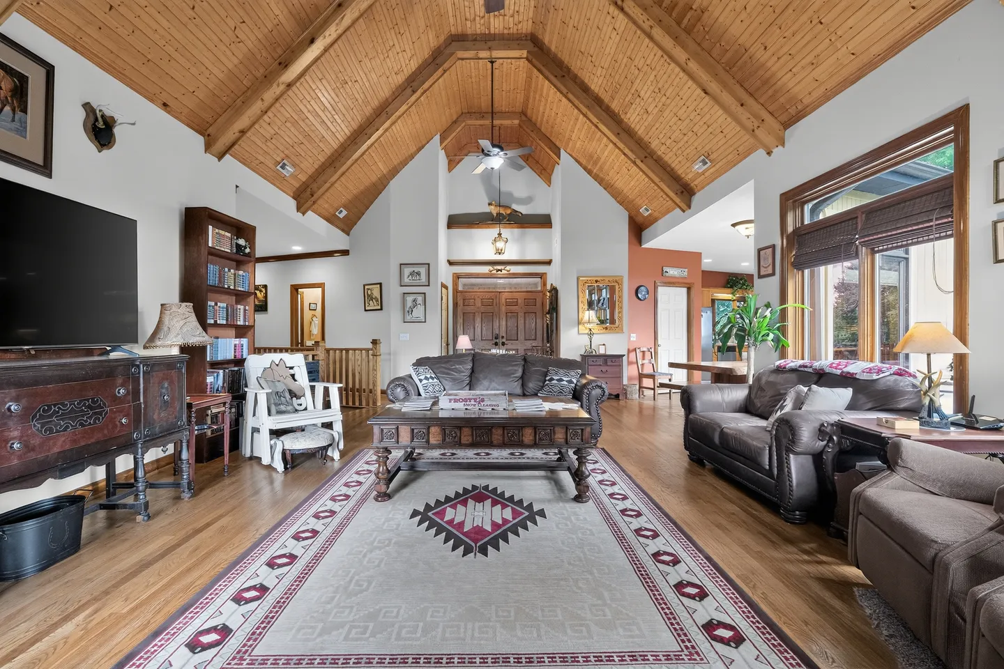 Living room with high wood-paneled cathedral ceilings, brown leather sofas, coffee table, and an area rug over wood flooring.
