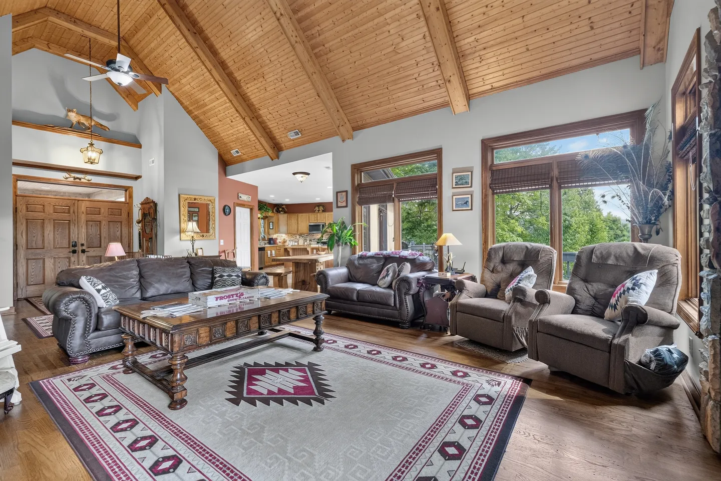Living room with vaulted wood-plank ceilings, wood floors, leather couches, armchairs, and large windows looking outside.