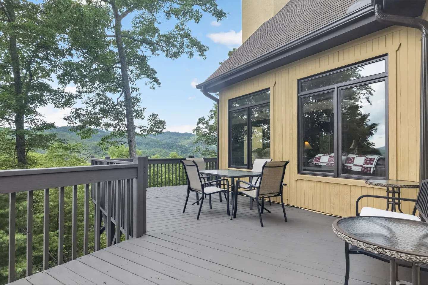 Open wooden deck with an outdoor dining table, chairs, and railings overlooking forested mountains.