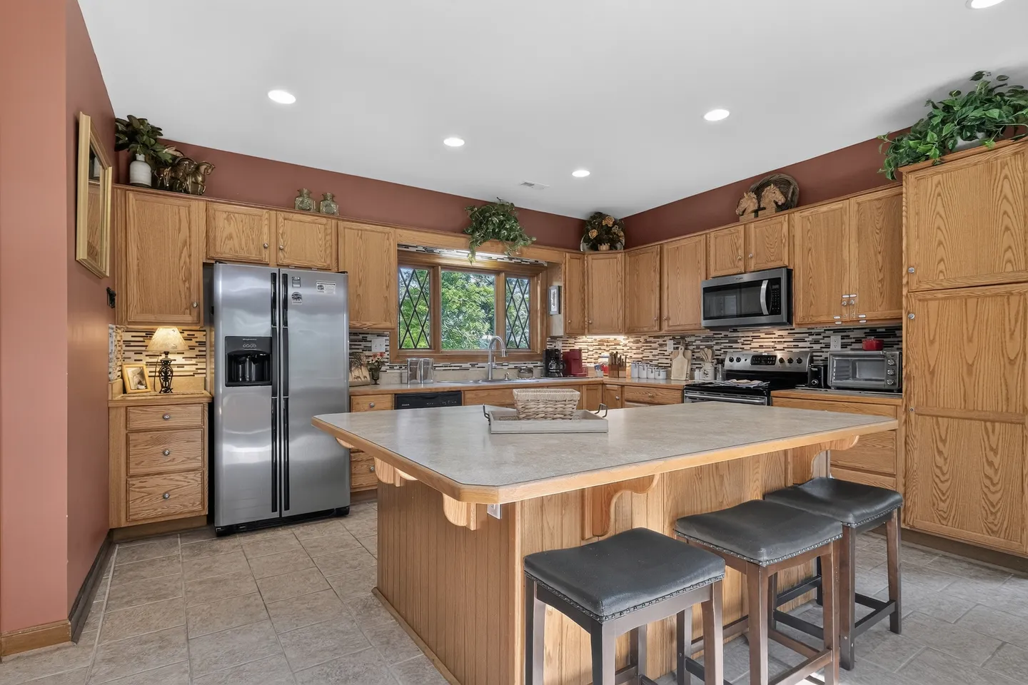 Spacious kitchen featuring light oak cabinetry, a large center island with barstools, stainless steel appliances, and tile flooring.
