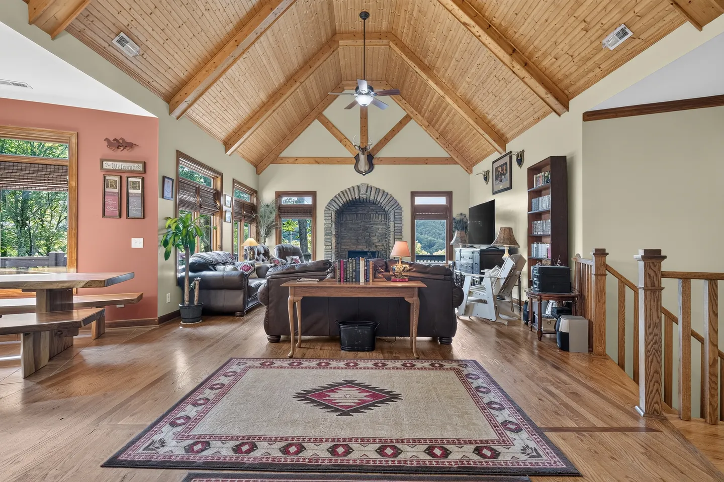 Spacious living room featuring high vaulted wood-paneled ceilings, a stone fireplace, leather seating, and hardwood floors.