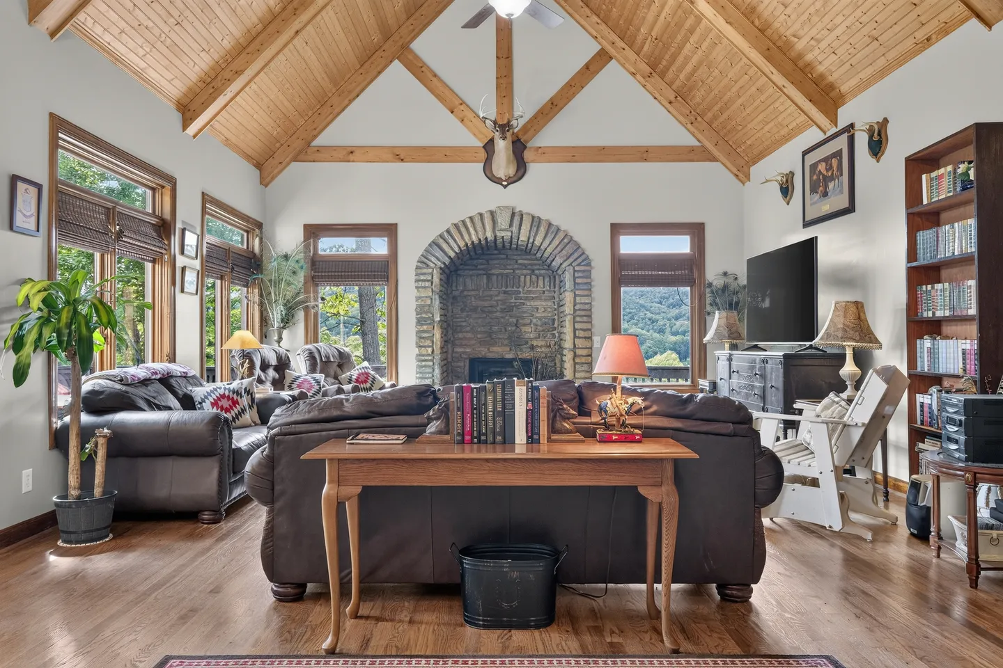 Living room with high wood-paneled cathedral ceilings, exposed beams, stone fireplace, and leather seating.