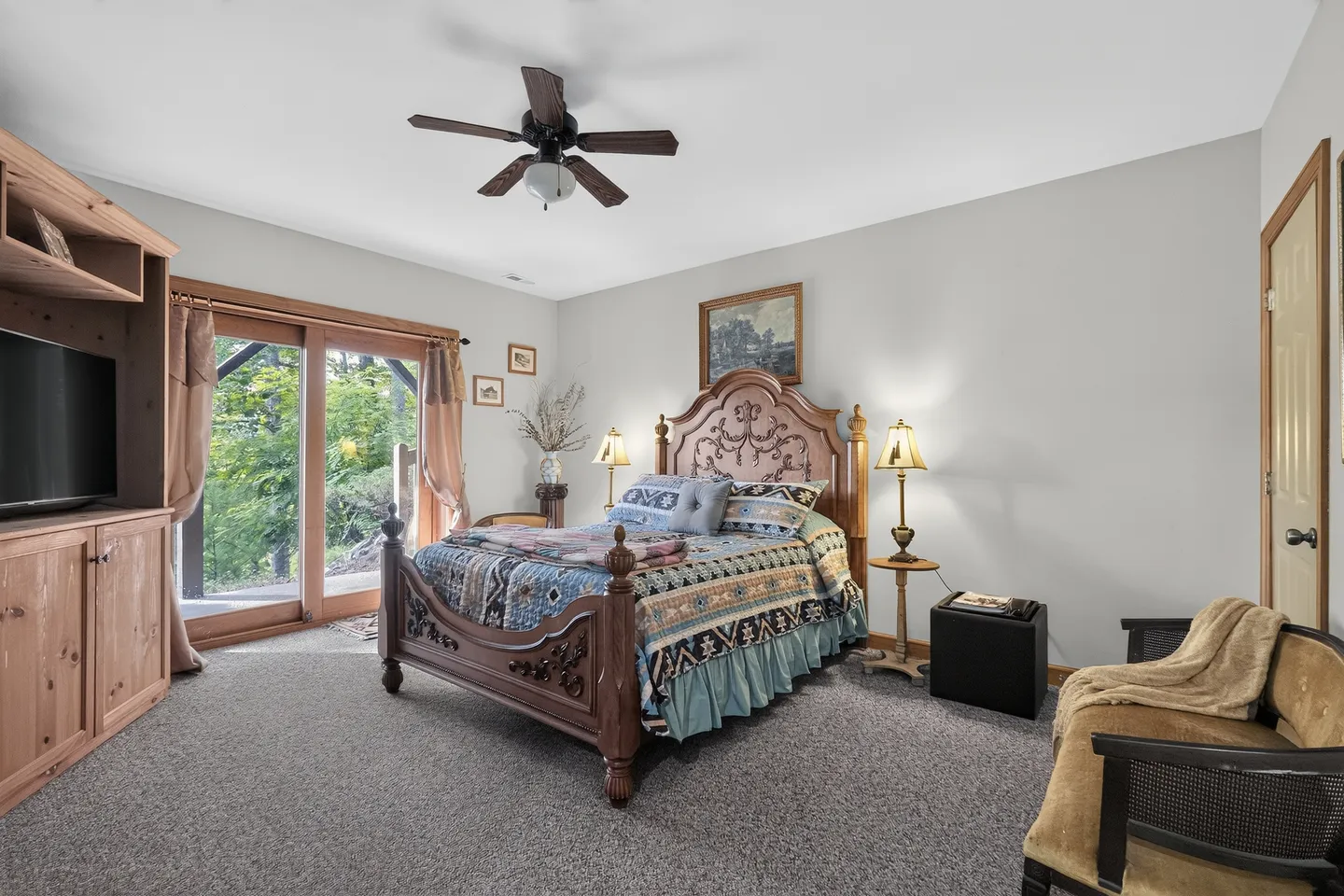 Bedroom with an ornate wooden bed, carpeted flooring, a ceiling fan, and sliding glass doors leading outside.