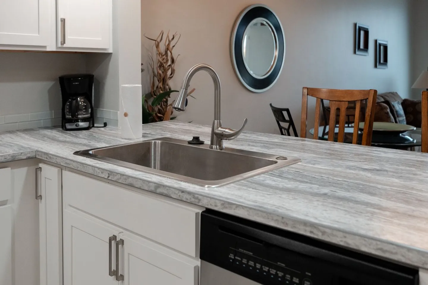 Close-up of a kitchen island counter featuring a stainless steel undermount sink, gooseneck faucet, and white cabinets.