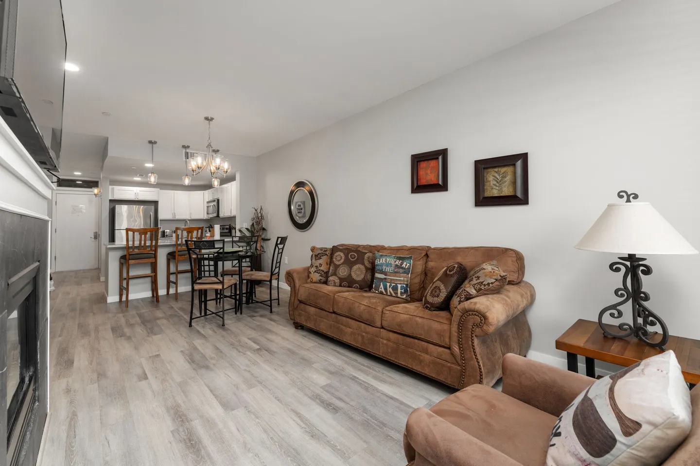 Open-concept living room with a brown sofa, fireplace, and view into the kitchen and dining area.