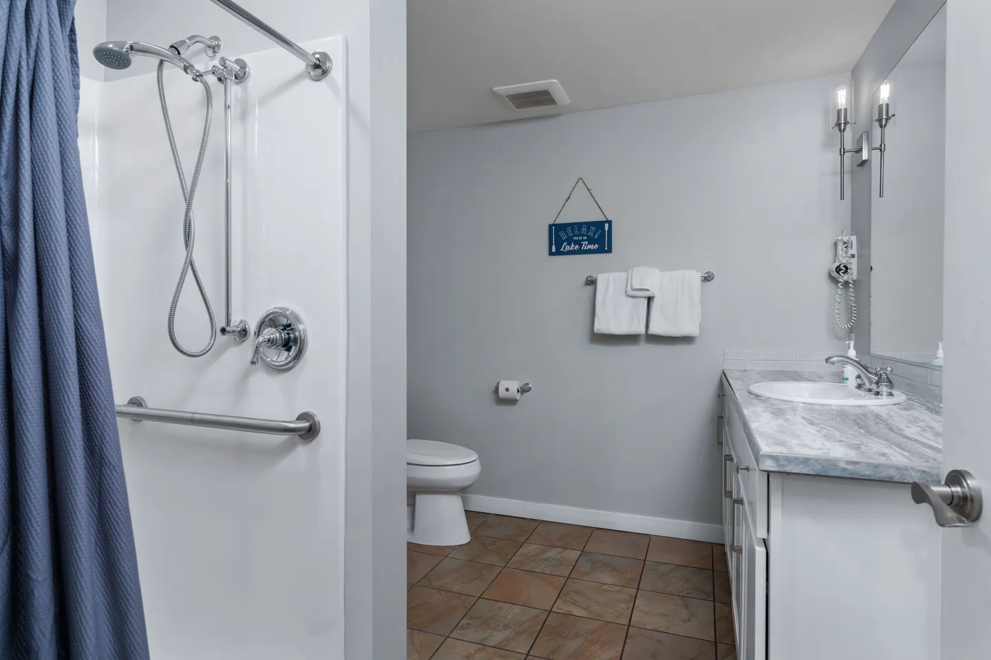 Bathroom with a walk-in shower on the left, a vanity with a marble-patterned countertop on the right, and a toilet in the center.