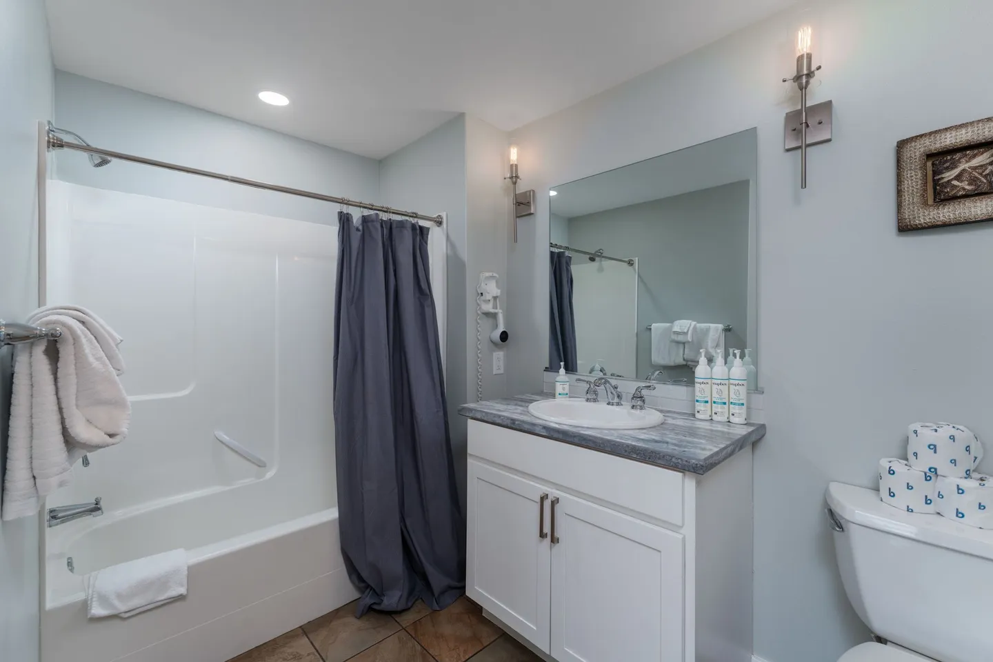 Bathroom featuring a white vanity with marble-patterned countertop, a framed mirror, a bathtub shower combination with a dark blue curtain, and a toilet.