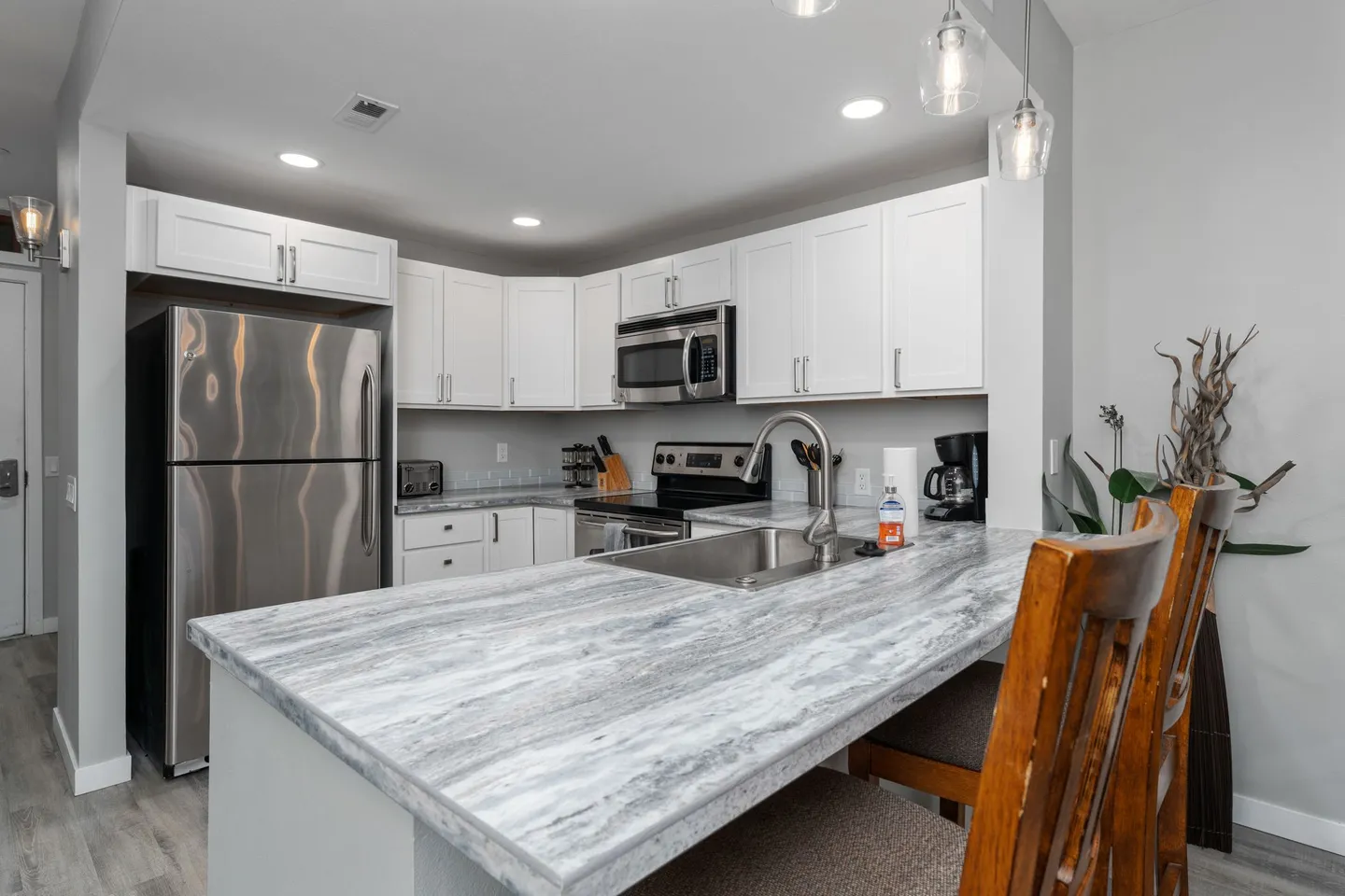 A kitchen with white cabinets, stainless steel appliances, and a marble-patterned island with a sink.