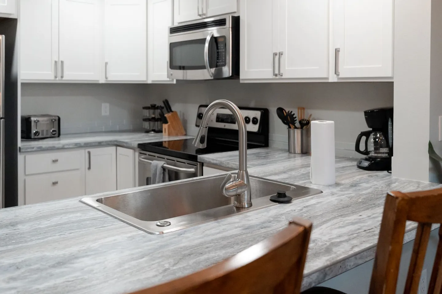 Close-up view of a kitchen island sink with stainless steel faucet, patterned countertops, and white cabinetry in the background.