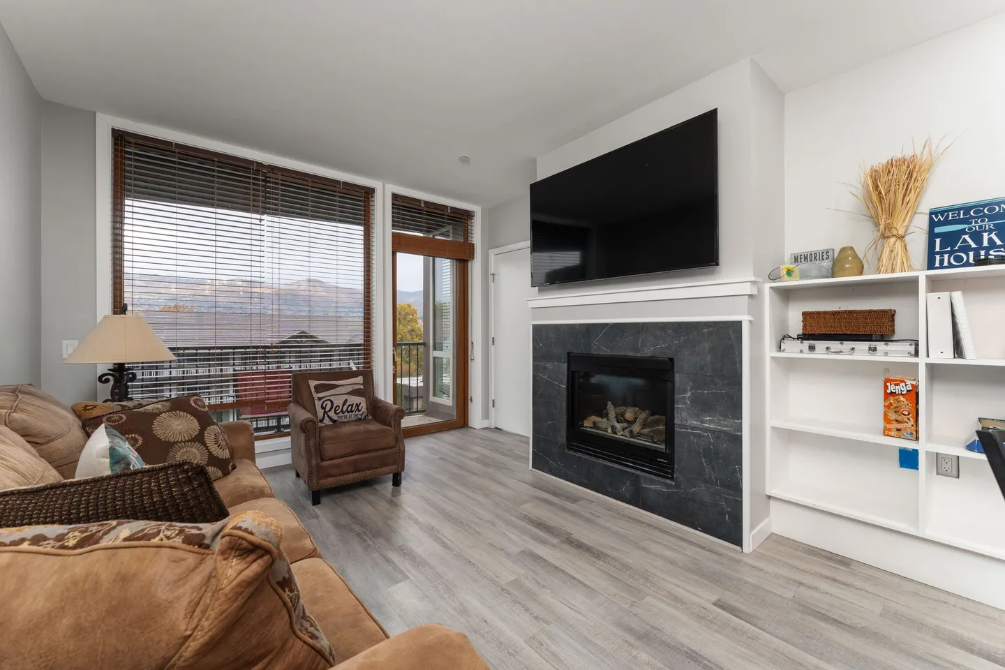 Living room with light-colored flooring, a leather sofa and armchair, a fireplace with dark surround, a mounted TV, and a door opening to a balcony.