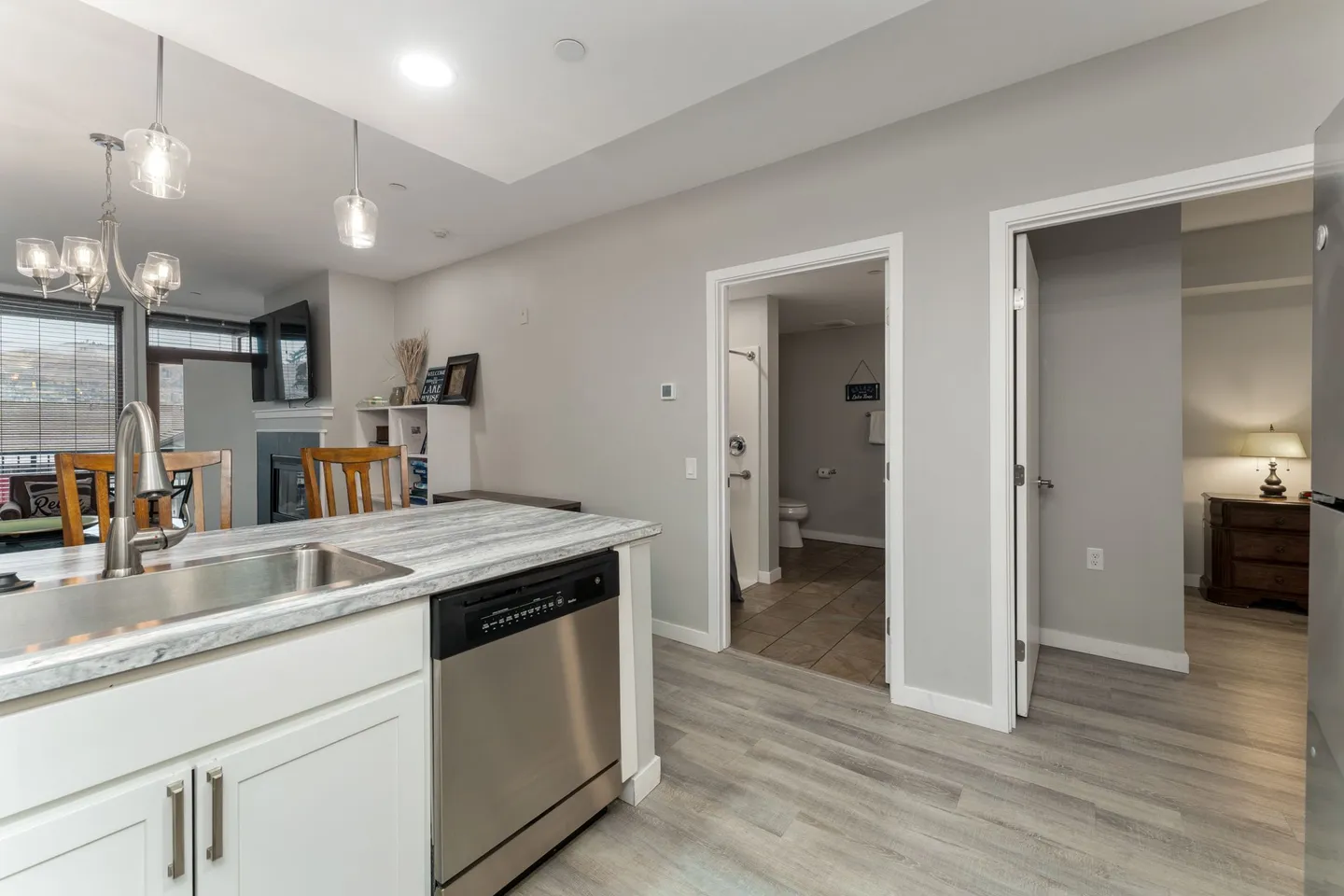 Kitchen island with a stainless steel dishwasher and sink looking toward a hallway with open doors to a bathroom and a bedroom.