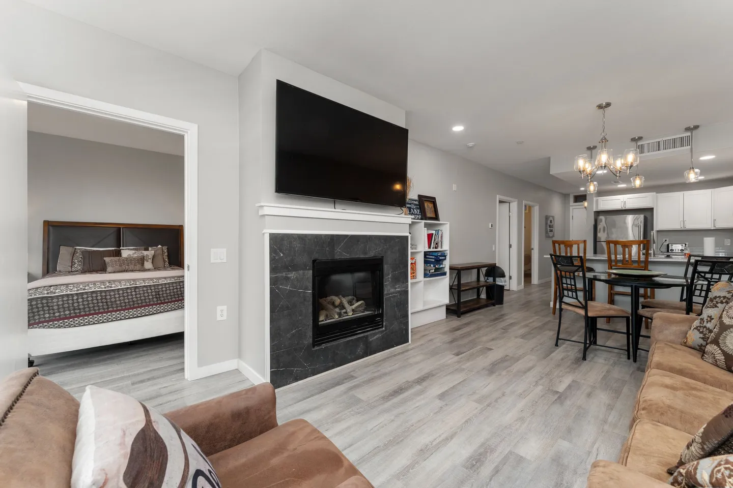 Open-concept living room with a fireplace, wall-mounted television, and views into a bedroom and adjacent dining area.