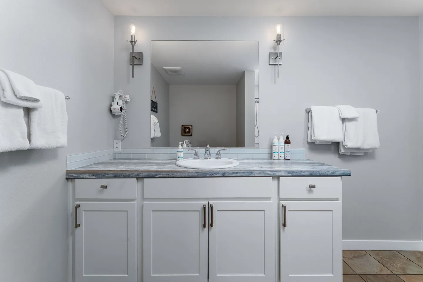 Bathroom vanity with white cabinets, patterned countertop, undermount sink, large mirror, and wall sconces.