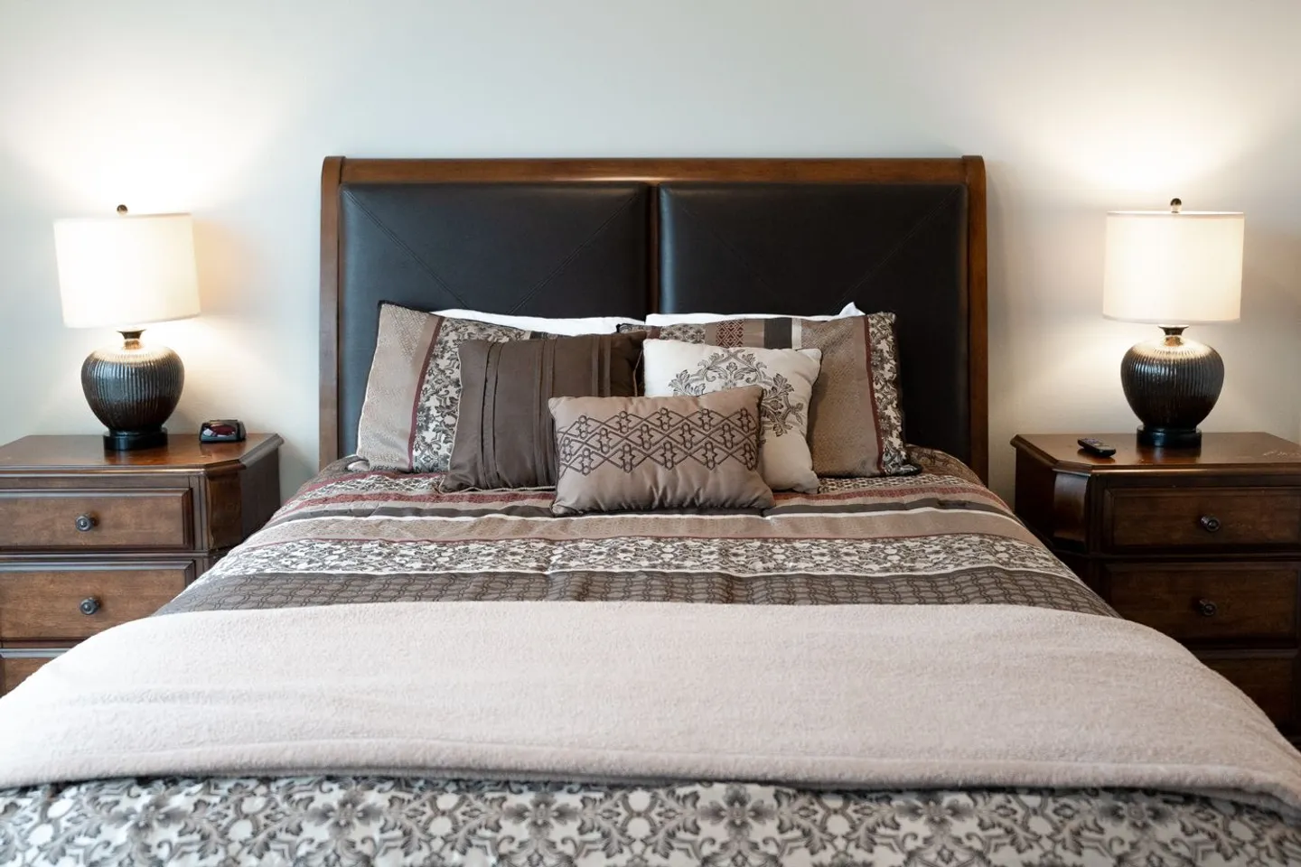 Bedroom featuring a made bed with dark headboard, decorative patterned pillows, and matching nightstands with illuminated lamps on each side.